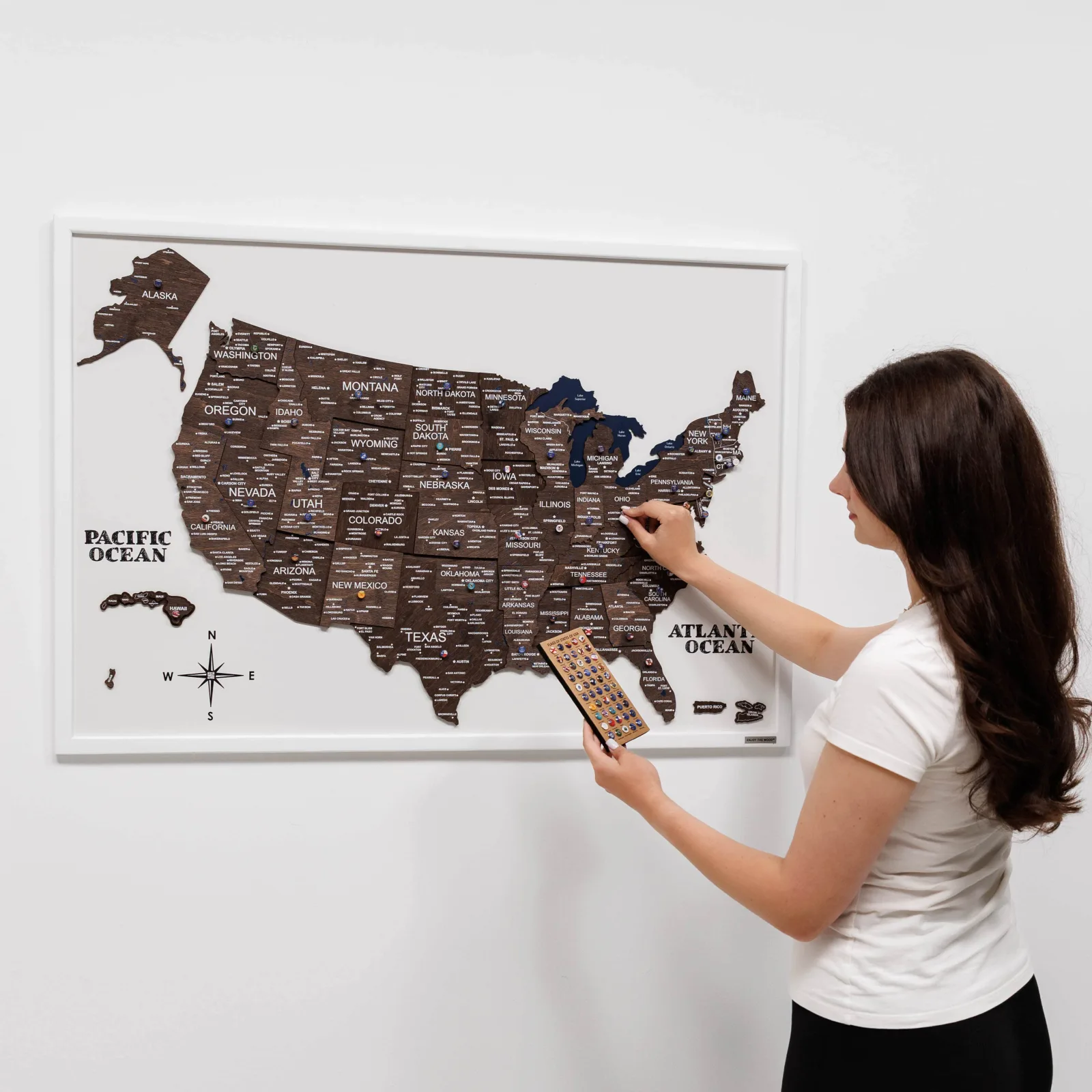 Framed dark wooden USA map with push pin tray on a white wall